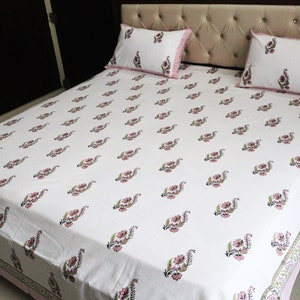 May include: White cotton bed sheet with a pink floral print. The sheet has a pink border and is shown on a bed with two matching pillowcases.