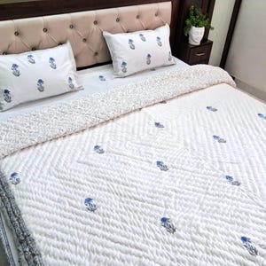May include: White quilted bedspread and pillow set with a blue floral pattern. The bedding features a tufted headboard and a patterned border. The pillows and bedspread have a repeating blue floral design.