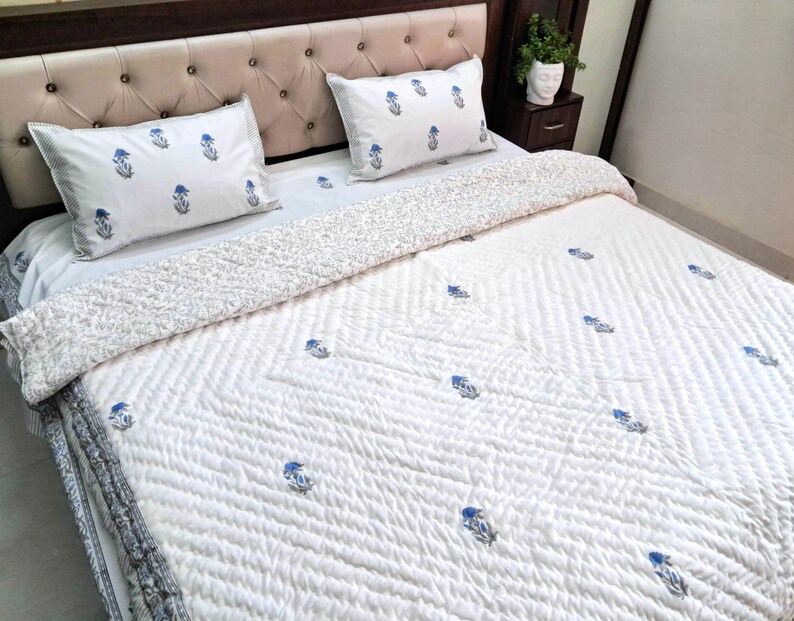 May include: White quilted bedspread and pillow set with a blue floral pattern. The bedding features a tufted headboard and a patterned border. The pillows and bedspread have a repeating blue floral design.