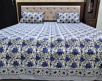 May include: A white and blue floral patterned bedspread and two matching pillowcases. The bedding features a repeating pattern of blue flowers and gray leaves on a white background. The bedspread has a striped border.