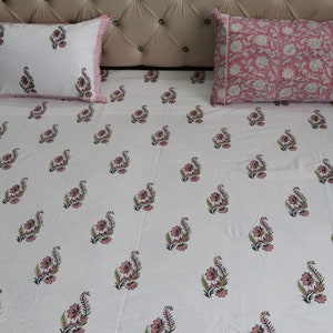 May include: White cotton bed sheet with a pink floral pattern. The sheet is on a bed with two matching pillowcases, one with a pink floral pattern and the other with a white floral pattern.