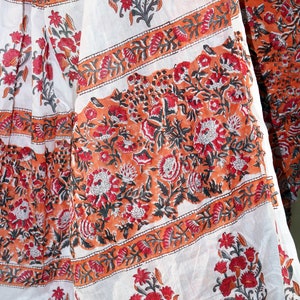 May include: White fabric with a floral print in shades of orange, red, and black. The fabric has a repeating pattern of flowers and leaves.