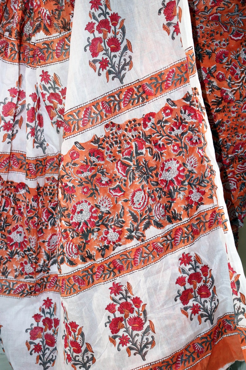 May include: White fabric with a floral print in shades of orange, red, and black. The fabric has a repeating pattern of flowers and leaves.