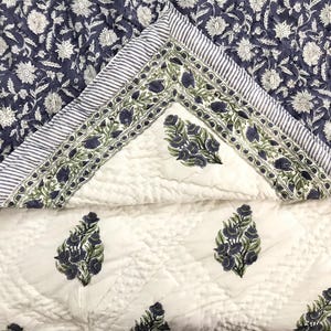 May include: A white cotton quilt with a blue floral pattern. The quilt has a quilted design and a border with a repeating floral pattern.