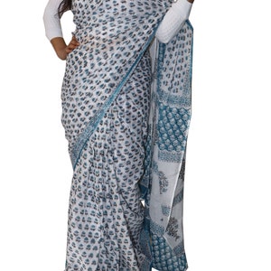 May include: A white cotton saree with a blue and brown floral print. The saree has a blue border with a geometric pattern.