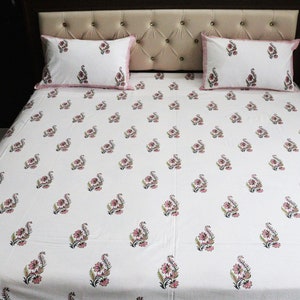 May include: White cotton bed sheet with a pink floral pattern. The sheet is on a bed with two matching pillowcases.