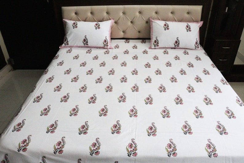 May include: White cotton bed sheet with a pink floral pattern. The sheet is on a bed with two matching pillowcases.