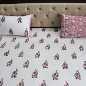 May include: White bed sheet with a pink floral pattern. The sheet has a pink and white border. Two matching pillowcases are on the bed.