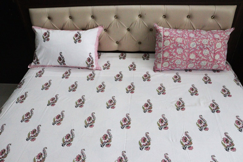 May include: White bed sheet with a pink floral pattern. The sheet has a pink and white border. Two matching pillowcases are on the bed.