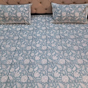 Könnte beinhalten: Bettwäsche-Set mit hellblauem Blumenmuster. Das Set beinhaltet ein Spannbetttuch, ein Bettlaken und zwei Kissenbezüge. Das Blumenmuster ist weiß und bedeckt die gesamte Oberfläche der Bettwäsche und Kissenbezüge.