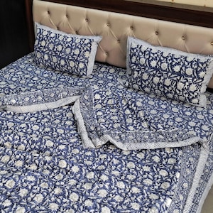 May include: A blue and white floral patterned bedspread set. The set includes a bedspread and two pillowcases. The floral pattern is white on a blue background. The pillowcases and bedspread have a striped border.