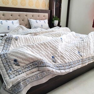 May include: A bed with a cream-colored quilted comforter and matching pillowcases. The comforter and pillowcases feature a blue floral pattern. The bed frame is dark brown, and the headboard is upholstered with cream-colored fabric.