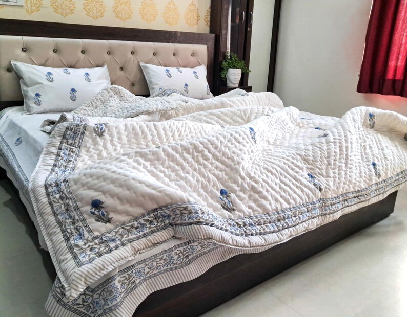 May include: A bed with a cream-colored quilted comforter and matching pillowcases. The comforter and pillowcases feature a blue floral pattern. The bed frame is dark brown, and the headboard is upholstered with cream-colored fabric.