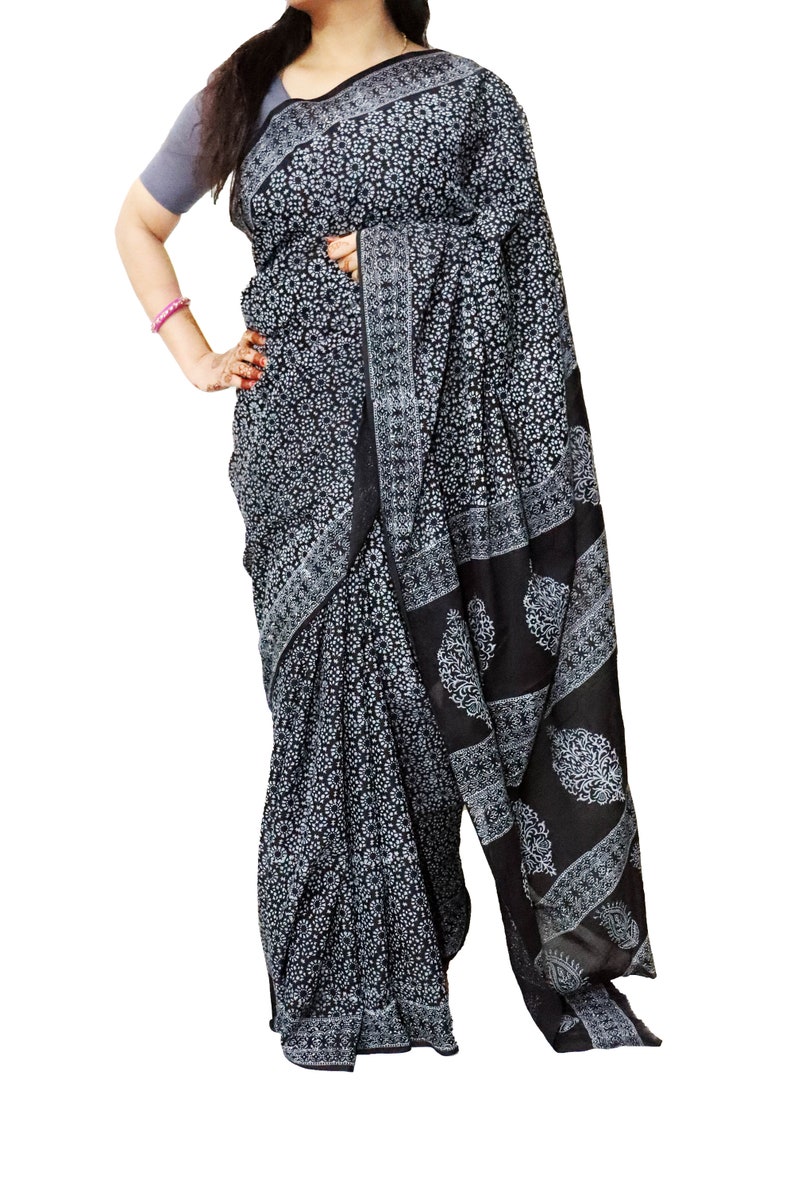 May include: A black and white cotton saree with a floral print. The saree is draped on a person and has a border with a paisley design.