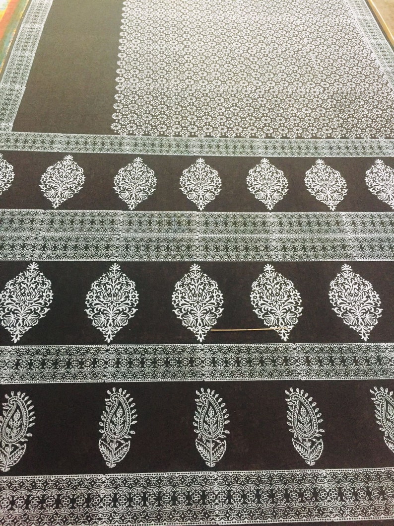 May include: A black fabric with a white floral pattern. The fabric has a repeating pattern of small white flowers and larger white floral designs.
