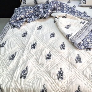 Puede incluir: Colcha de algod&oacute;n blanco con un patr&oacute;n de diamante y estampado floral negro. La colcha est&aacute; doblada por la mitad y tiene un estampado floral azul y blanco en el reverso.