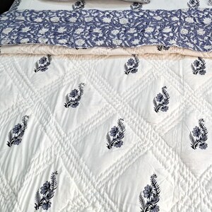 Puede incluir: Edred&oacute;n de algod&oacute;n blanco con un patr&oacute;n de diamante y estampado floral negro. El edred&oacute;n est&aacute; doblado por la mitad, mostrando el lado trasero, que es un estampado floral azul claro.