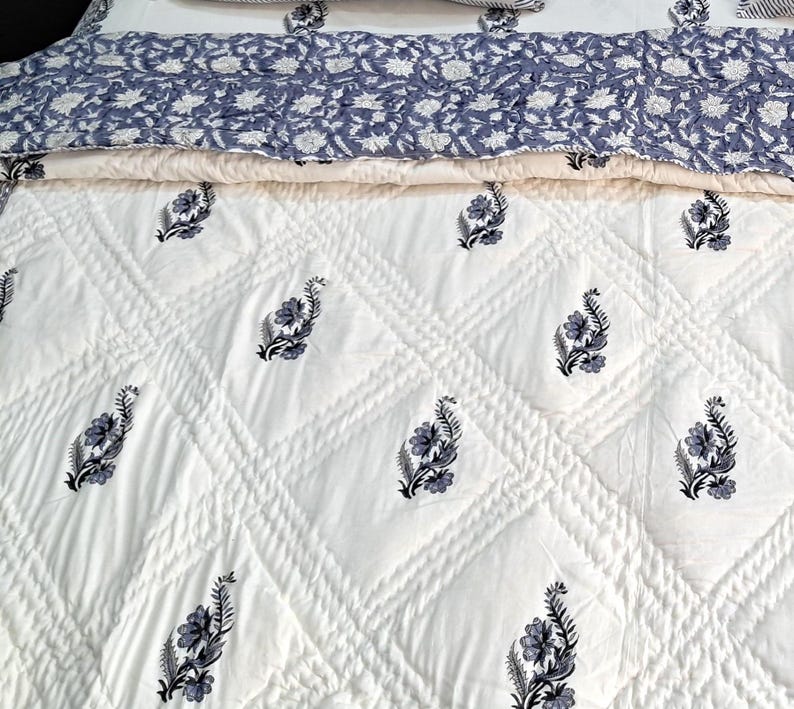 Puede incluir: Edred&oacute;n de algod&oacute;n blanco con un patr&oacute;n de diamante y estampado floral negro. El edred&oacute;n est&aacute; doblado por la mitad, mostrando el lado trasero, que es un estampado floral azul claro.