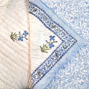 May include: A white cotton quilt with a blue floral pattern. The quilt is made up of two panels, one with a smaller floral pattern and the other with a larger floral pattern.