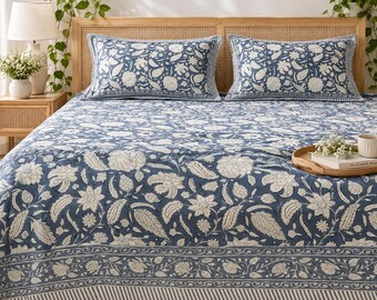 May include: A blue and white floral print bedspread set featuring two matching rectangular pillows. The fabric displays a repeating pattern of stylized flowers and leaves with a decorative border along the bottom edge of the bedspread.