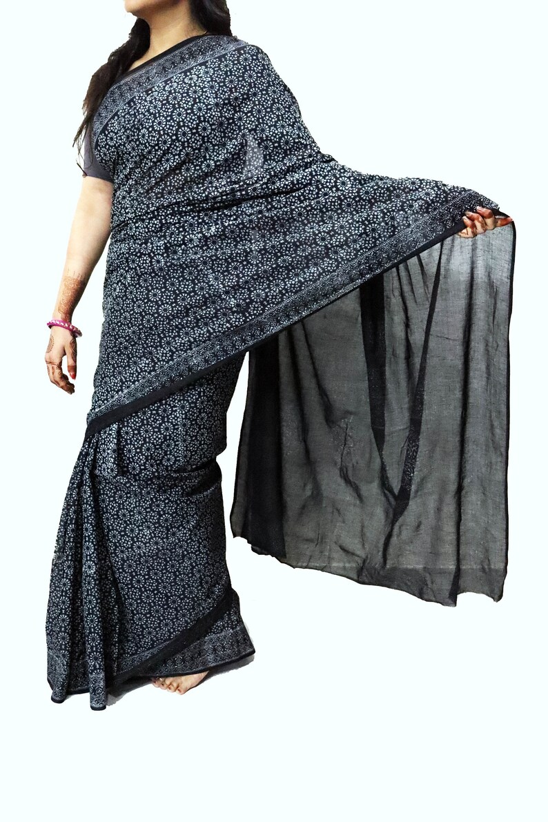 May include: A black and white patterned saree with a black sheer pallu. The saree features a floral design and is draped around a person.