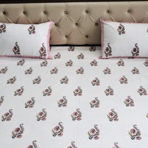 May include: White cotton bed sheet with a pink and green floral print. The sheet has a pink and white border and comes with two matching pillowcases.