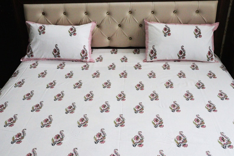 May include: White cotton bed sheet with a pink and green floral print. The sheet has a pink and white border and comes with two matching pillowcases.