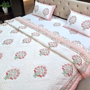 May include: White floral patterned bedding set with a quilted comforter, two pillowcases, and a fitted sheet. The floral design features red and green accents. The bedding set has a pink striped border.