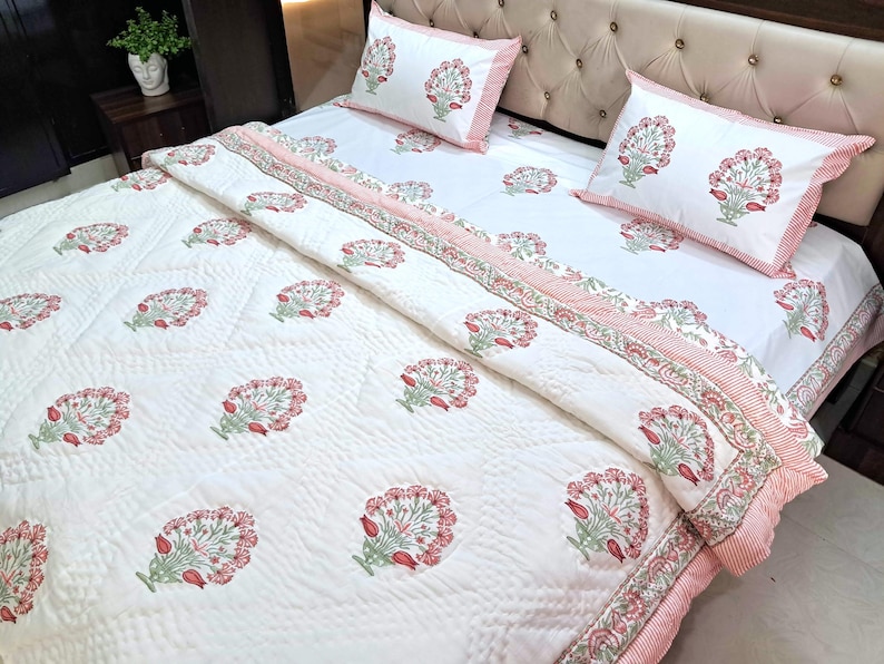 May include: White floral patterned bedding set with a quilted comforter, two pillowcases, and a fitted sheet. The floral design features red and green accents. The bedding set has a pink striped border.