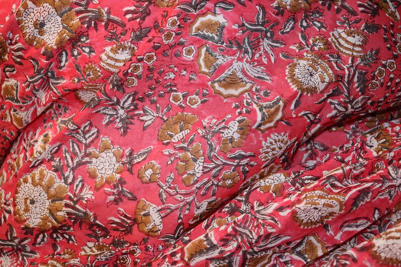 May include: Red fabric with a floral print in brown and white. The fabric has a textured, slightly wrinkled appearance.