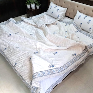 May include: White bedspread and pillow set with a blue floral pattern. The quilt has a stitched design and a blue border. Two matching pillows are visible on the bed.