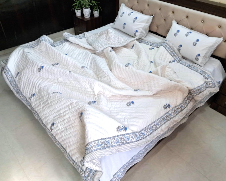 May include: White bedspread and pillow set with a blue floral pattern. The quilt has a stitched design and a blue border. Two matching pillows are visible on the bed.