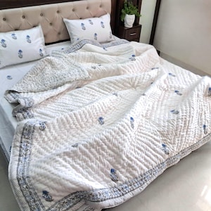 May include: White quilted bedspread with blue floral accents and matching pillowcases. The bedding features a detailed pattern and a decorative border. The bed is made up with the quilt and pillows.