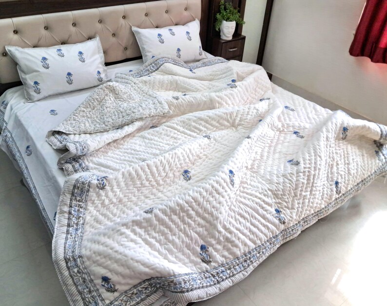 May include: White quilted bedspread with blue floral accents and matching pillowcases. The bedding features a detailed pattern and a decorative border. The bed is made up with the quilt and pillows.