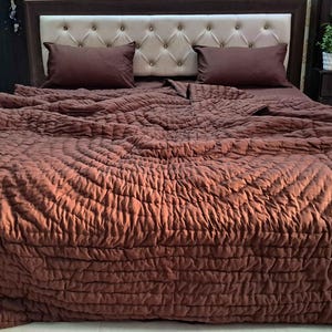 May include: A bed featuring a brown quilted duvet cover and matching pillows. The headboard is upholstered in a light beige fabric with a button-tufted design. The bedding creates a warm and inviting atmosphere.