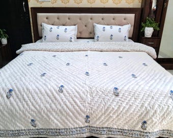 May include: White quilted bedspread with blue floral accents. The bedspread features a repeating pattern of blue flowers and a decorative border. Two matching pillowcases with blue floral designs are visible.
