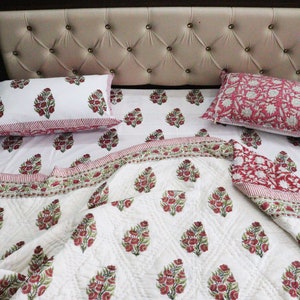 May include: A white cotton quilt with a pink and green floral print. The quilt is folded on a bed with matching pillowcases.