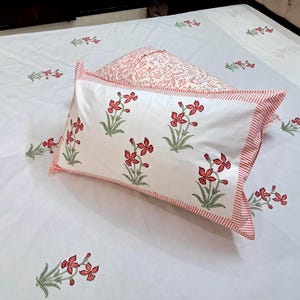 May include: White bedding set with a floral pattern in red and green. The set includes a pillowcase with a red and white striped border and a matching floral design. The bedsheet also features the same floral pattern.