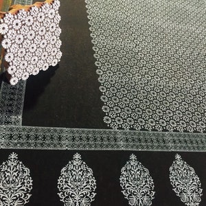 May include: A black fabric with a white floral pattern printed on it. A wooden block with a floral design is used to create the pattern.