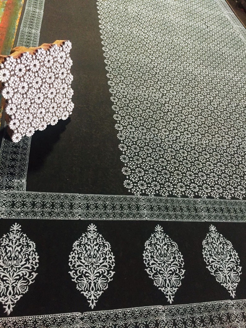 May include: A black fabric with a white floral pattern printed on it. A wooden block with a floral design is used to create the pattern.