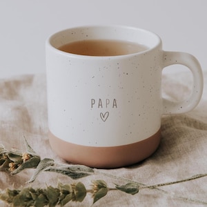 Puede incluir: Taza de cerámica blanca con borde marrón, llena de un líquido marrón claro. La taza tiene la palabra "PAPA" y un corazón impreso.