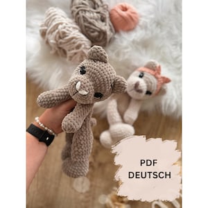 Könnte beinhalten: Zwei handgefertigte Häkel-Plüschtiere aus weichem, strukturiertem braunem und beigem Garn. Ein Tier hat einen braunen Körper mit dunklen Augen und weißer Schnauze, das andere ist beige mit pfirsichfarbenem Stirnband. Text: PDF DEUTSCH.