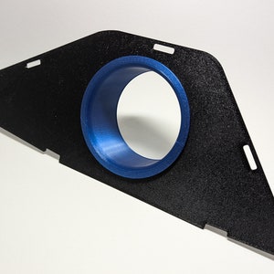 Pode incluir: Uma peça triangular de plástico preto com um anel de plástico azul no centro. O anel tem um furo no centro.