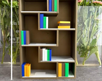 Könnte beinhalten: Ein kleines, braunes, abgestuftes Bücherregal mit weißen Regalböden, ca. 11 cm breit und 21 cm hoch. Es enthält mehrere Miniaturbücher in verschiedenen Farben. Rosa Blumen in einer durchsichtigen Vase sind im Hintergrund.
