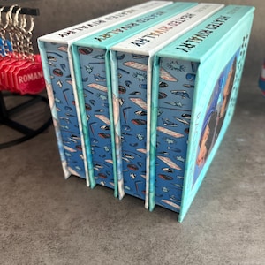 May include: Four books titled "Heated Rivalry" are stacked together. The book spines are white with teal text. The book covers are teal with a pattern of sports equipment. The book's edges are teal.