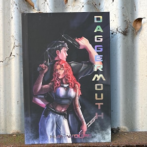 May include: A book titled Dagger Mouth by H.M. Wolfe featuring a cover illustration of two individuals standing back-to-back. One person has long wavy red hair and wears a white top, while the other has dark hair and holds a black handgun.