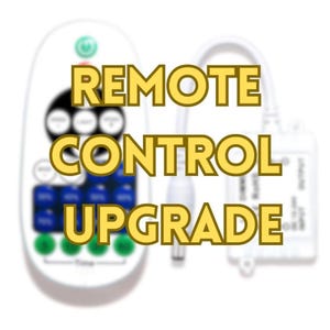 May include: White remote control with multiple buttons and the text "REMOTE CONTROL UPGRADE" in yellow. The remote has blue and green buttons. A white cable and a small white device are also visible.