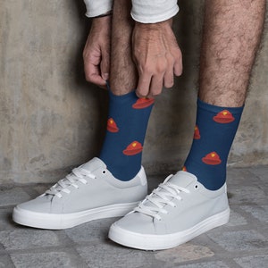 May include: A pair of grey trainers with white laces and a navy blue sock with a red fire hat pattern.