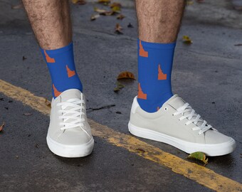 May include: A pair of blue socks with an orange outline of the state of Idaho repeated on them. The socks are being worn by a person with white trainers.