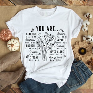 May include: White t-shirt with black text and floral design. The text reads "You are... Beautiful, Victorious, Enough, Created, Strong" and "Amazing, Capable, Chosen, Never Alone, Always Loved".